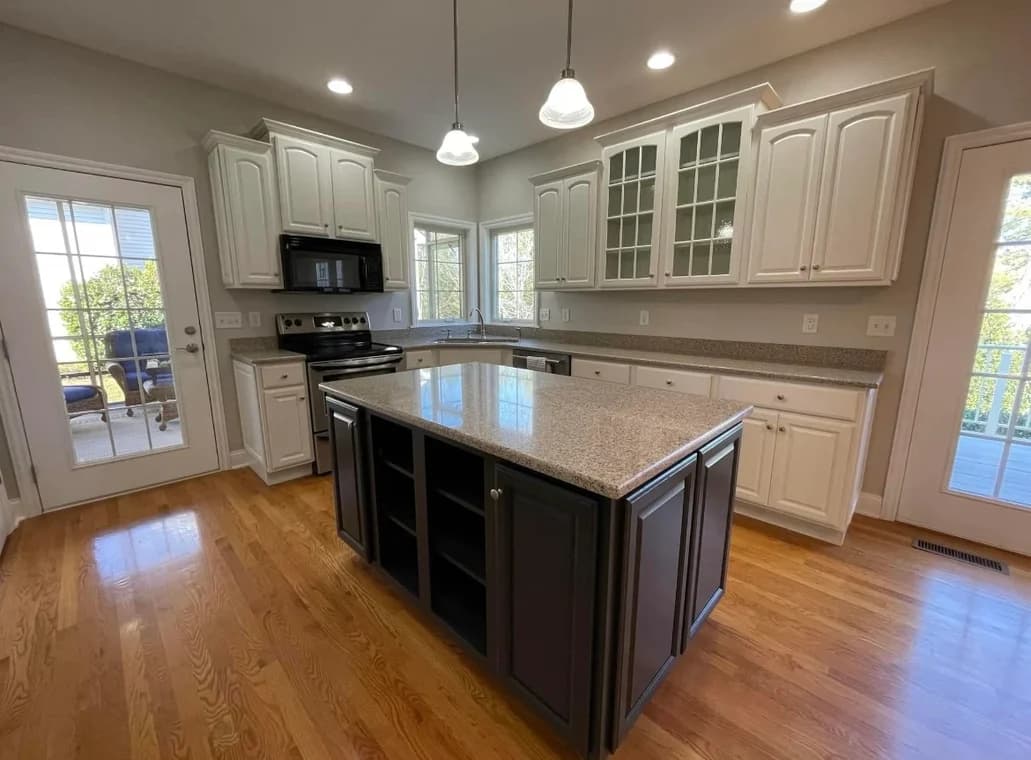 "This is an image from Prestige Pro Painters, located in Texas. The kitchen features freshly painted white cabinets, a dark island base, granite countertops, and pendant lighting above the island."