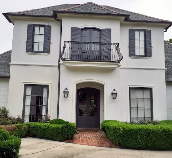 This is an image from Ozuna’s Painting Inc., located in Louisiana. The photo shows a two-story home with a smooth white exterior, dark gray shutters and doors, and elegant wrought iron balcony accents, demonstrating the company’s refined exterior painting craftsmanship.