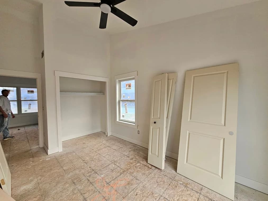 This is an image from Great Lakes 1-800 Painting LLC company, located in Davison, MI The image is a residential interior painting in progress by Great Lakes Painting, featuring white walls, trim, and ceiling with doors removed for painting preparation in a bedroom with a black ceiling fan.
