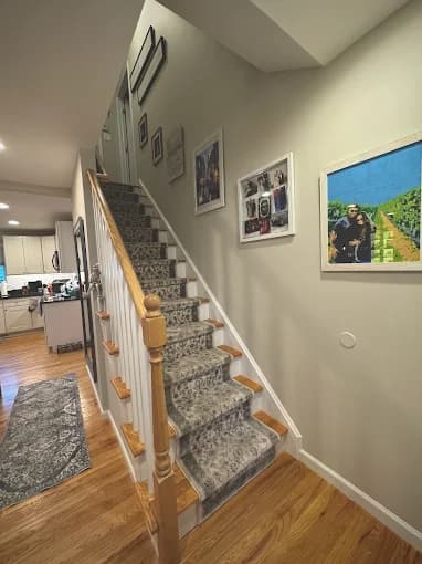 This is an image from Anthony's Painting & Decorating, Inc., located in New York. The photo shows a staircase area with freshly painted light-gray walls, framed photos, and a carpeted runner on wooden steps.