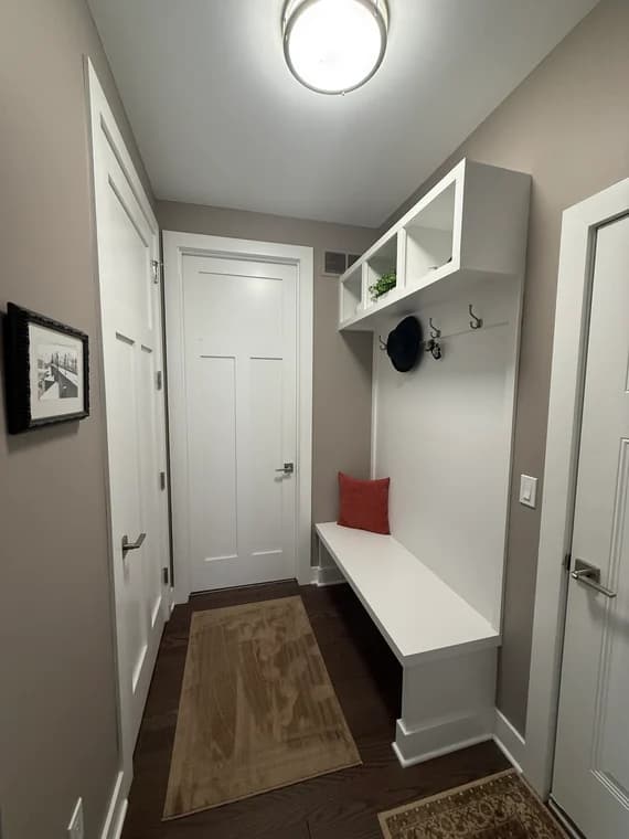 This is an image from MacFarland Painting - Ann Arbor company, located in Ann Arbor, MI The image is a modern mudroom with white built-in bench, storage cubbies, and hooks, painted in soft beige and white by MacFarland Painting.