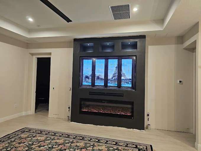 This is an image from Fresh Look Painting company, located in Sarasota, FL. The image is a modern living room with custom black accent wall featuring recessed lighting, electric fireplace, and mounted TV, painted by Fresh Look Painting LLC