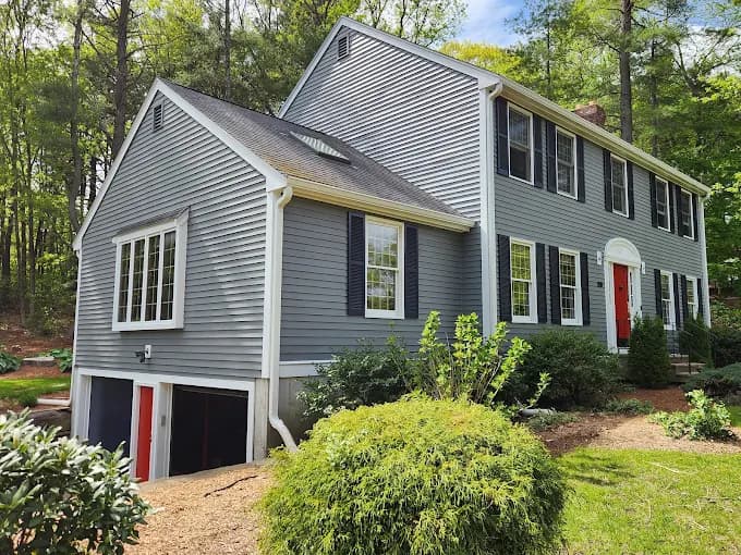 This is an image from WM Painting & More, located in Massachusetts. The photo shows a two-story colonial-style home with freshly painted gray siding, white trim, black shutters, and a bright red front door.