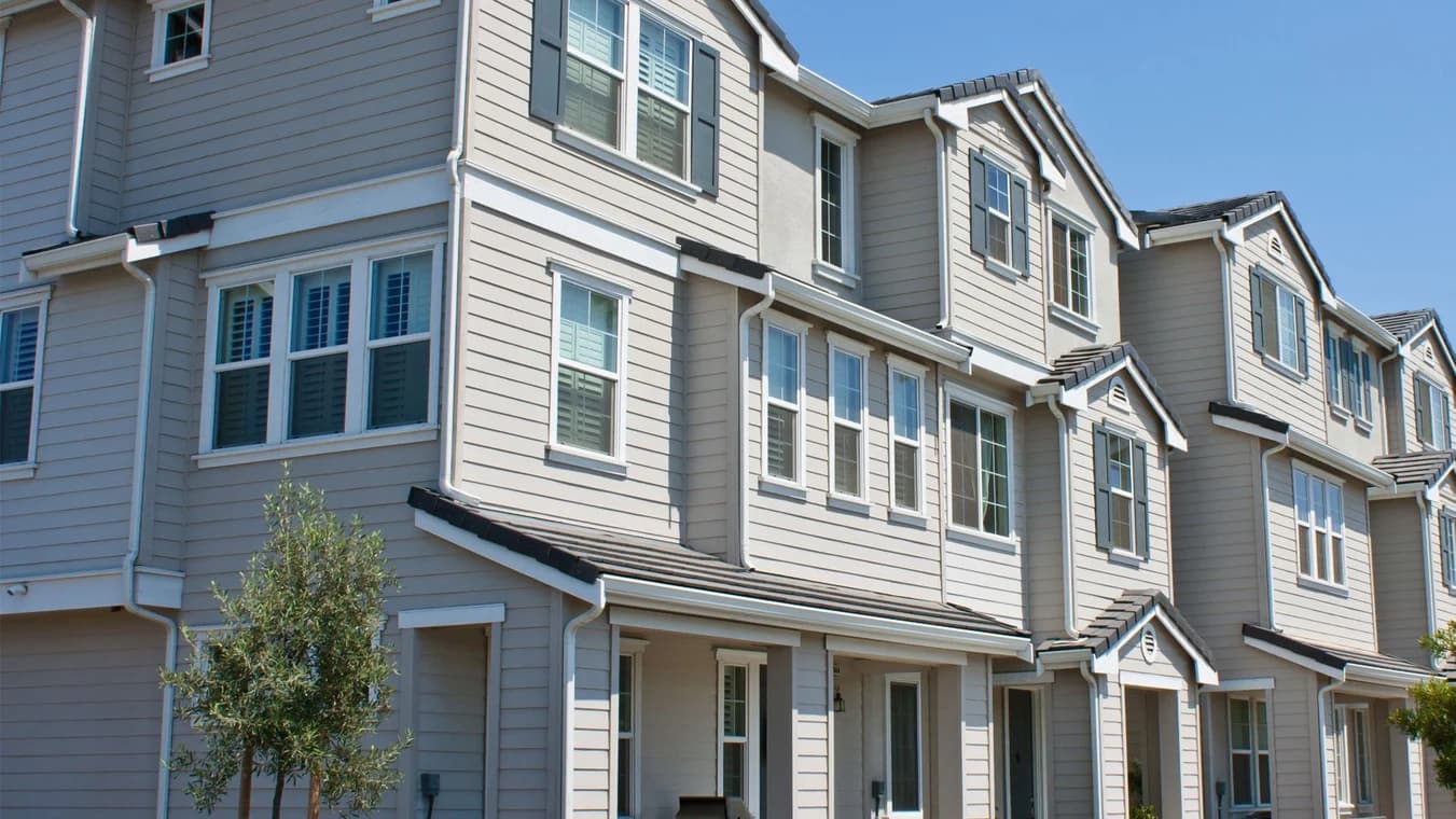 A row of modern beige townhouses painted with clean, uniform siding and white trim