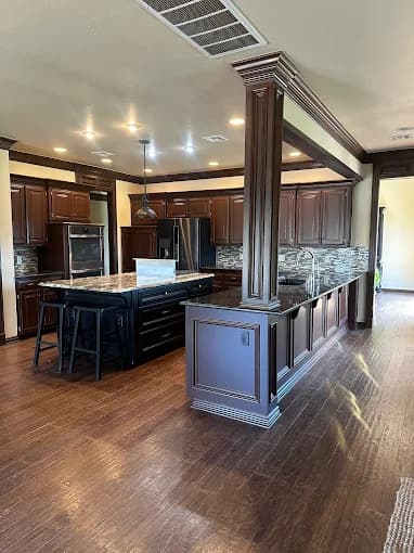 This is an image from Legacy Painting, located in Oklahoma. The photo shows a modern kitchen with dark wood cabinetry, a large island with bar seating, stainless steel appliances, and decorative backsplash tile.