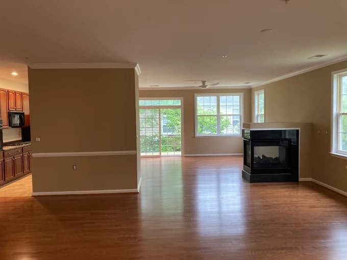 This is an image from CertaPro Painters of Southern Maryland, located in Maryland. The photo shows a freshly painted open-concept living area with tan walls, white trim, hardwood floors, and a modern black fireplace.
