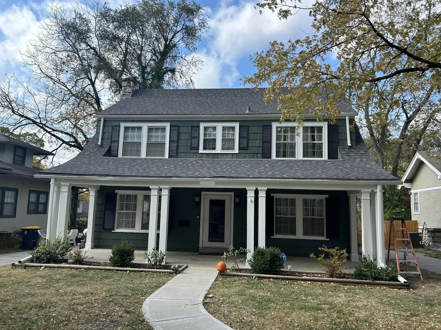 This is an image from Mission Painting and Home Improvements. The image shows a two-story home with freshly painted dark green siding and white trim, highlighting professional exterior painting work.