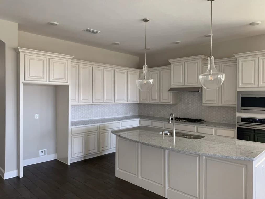 "This is an image from All Seasons Painting LLC, located in Texas. The kitchen features cream-colored raised-panel cabinets, granite countertops, a patterned backsplash, and pendant glass lighting over a large island."