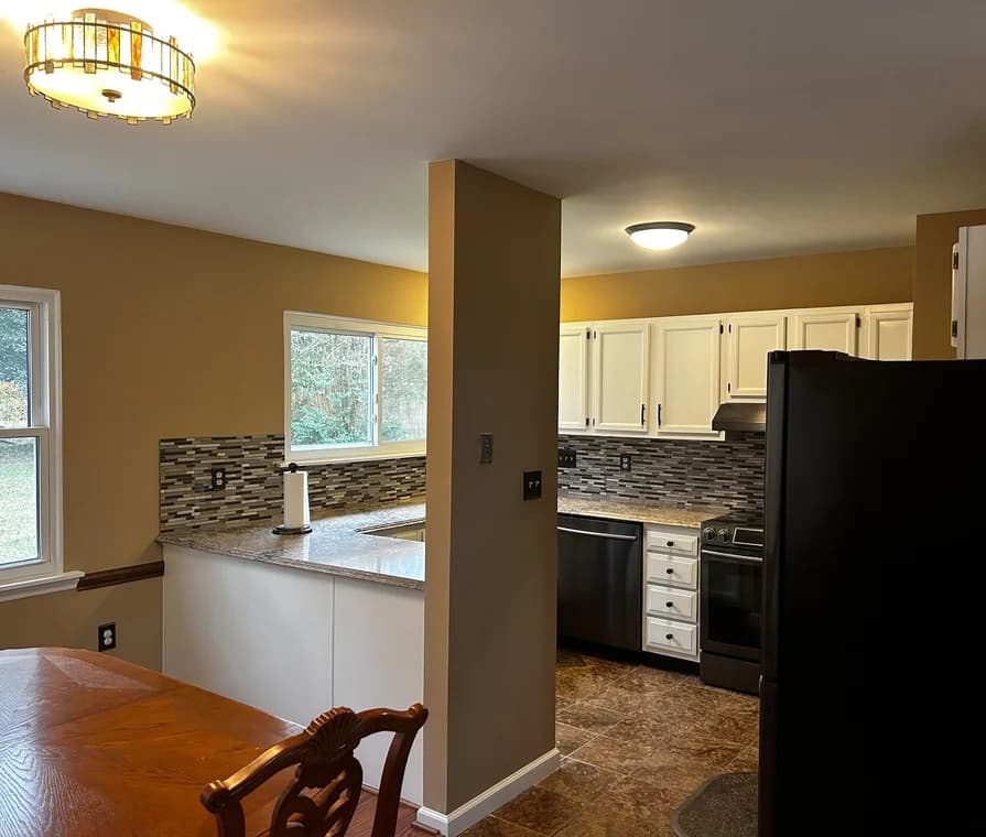 This is an image from Charlotte Pro Painters, located in North Carolina. This is a kitchen with white cabinets, granite countertops, and tiled backsplash, freshly painted walls in a warm tan shade.