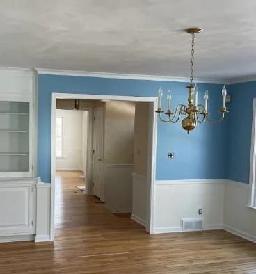 Interior painting project by Michael's Painting Service in Rockford, IL. The image shows light blue dining room walls, white trim, hardwood floors, and a brass chandelier.