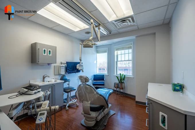 This is an image from Paint Bros MA, located in Massachusetts. The photo shows a freshly painted dental office with light gray walls, white trim, and polished wood flooring, creating a bright and modern clinical environment.