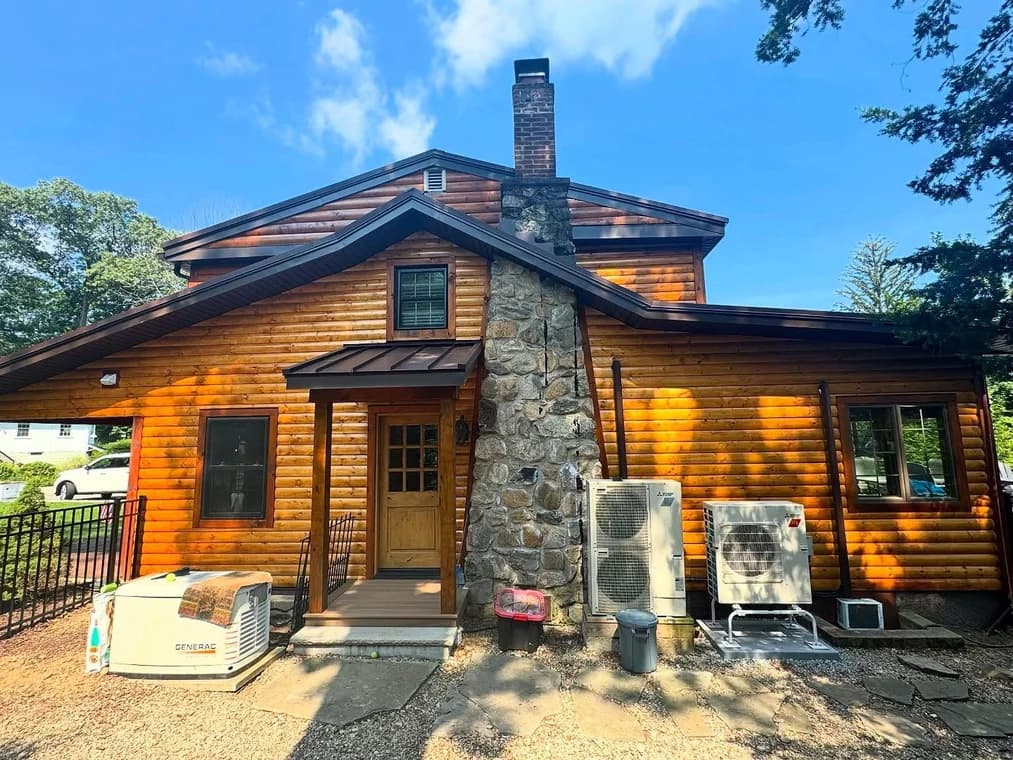 This is an image from That 1 Painter North Jersey. It shows a log cabin style home with a stone chimney and newly refinished wood siding for a natural look.