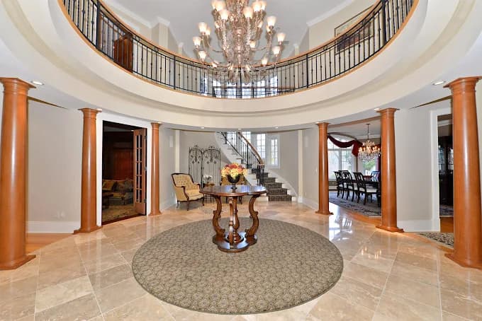 This is an image from Spectrum Painting, located in New Jersey. The photo shows a grand foyer with a circular layout, marble tile flooring, a large chandelier, and wood columns surrounding the entry space.