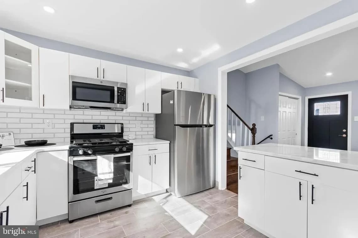 A finished basement painted in light gray with white trim, featuring recessed ceiling lights, carpeted flooring, and built-in white shelving.