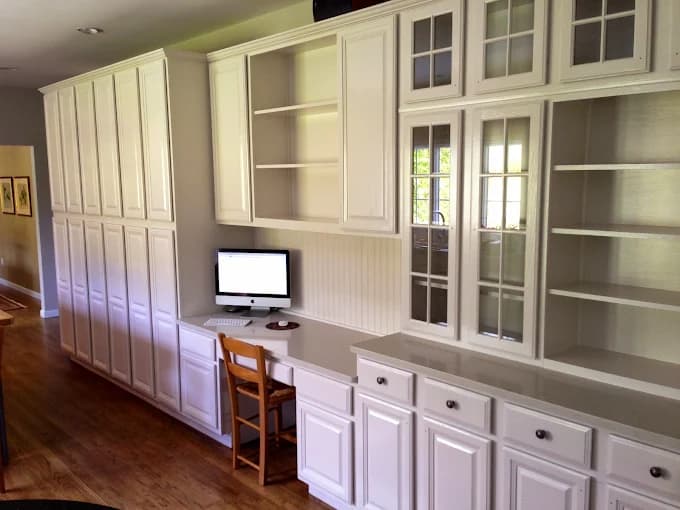 This is an image from Firefly Painting Inc, located in Colorado. The photo shows a built-in office wall with freshly painted white cabinetry, shelving, and a desk area with a wood chair and computer.