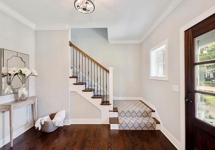 "This is an image from Roll City Painting, located in Texas. The photo shows a bright, clean entryway with hardwood floors, a patterned stair runner, and light gray walls."