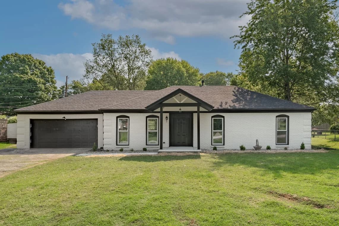 This is an image from Gomez Painting LLC, located in Kentucky. The exterior shows a freshly painted single-story home with white brick walls, black trim, and a dark roof under a bright blue sky.