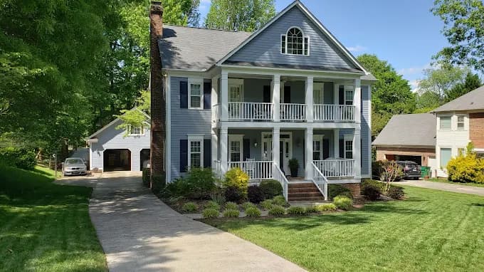 Exterior painting project by DeHaan Painting in Charlotte, NC. The image shows a gray two-story home with white trim, porch columns, and a front lawn.