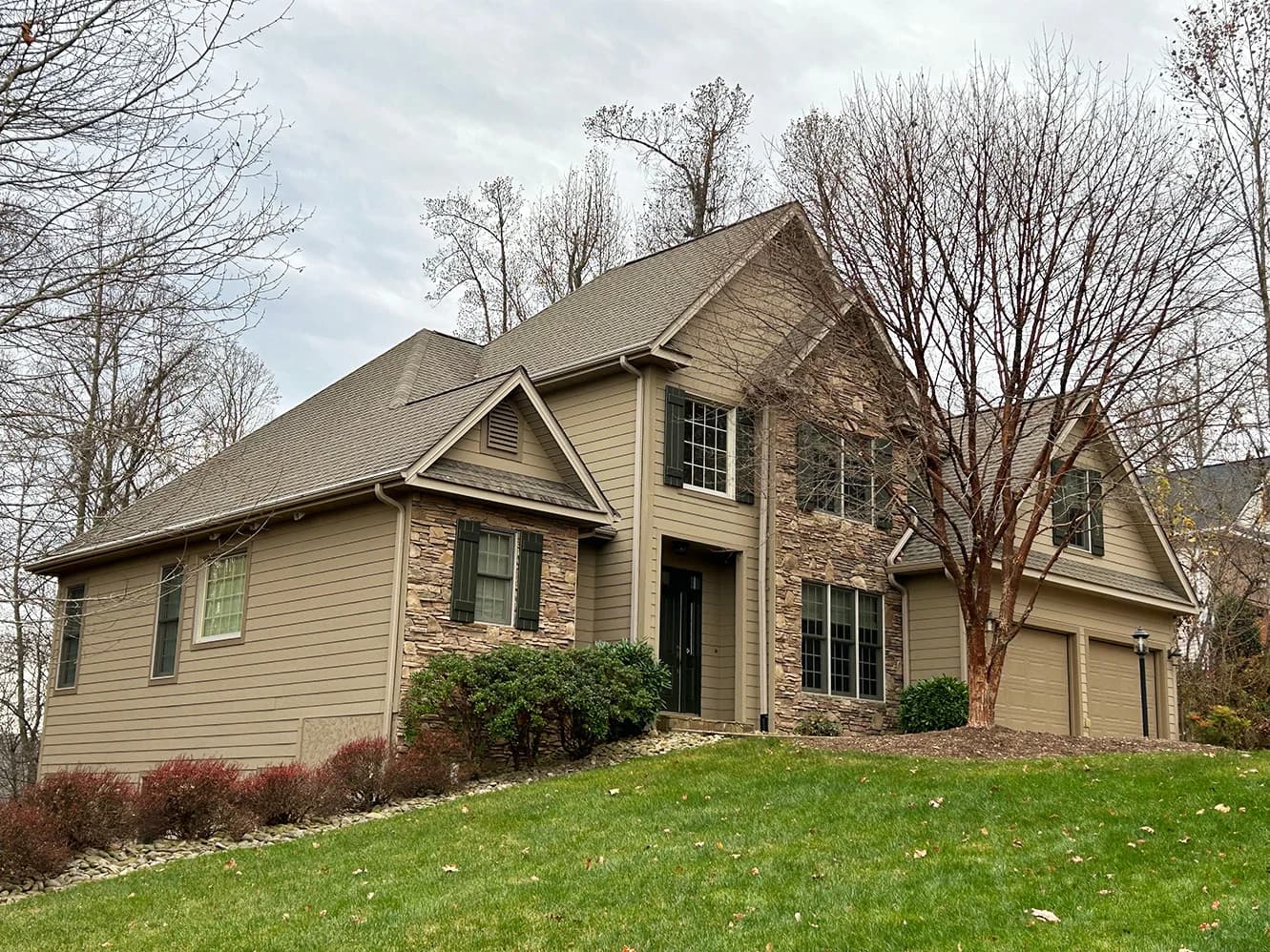 Exterior painting project by Burlett Painting, LLC in Hendersonville, North Carolina. The image shows a tan two-story home with stone accents and dark shutters.