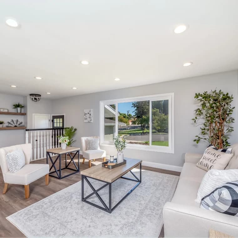 This is an image from LA Painting, located in Louisiana. The image shows a bright, freshly painted living room with light gray walls, white trim, and modern décor featuring neutral furniture, wood floors, and natural light from a large front window.