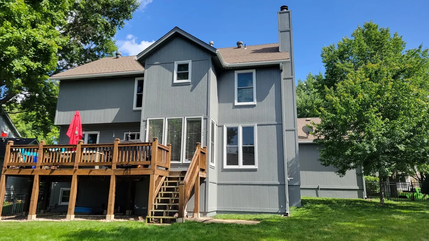 This is an image from Stack Painting. The image is the exterior rear view of a two-story home in Kansas City KS with gray siding, white trim, and a wooden elevated deck.