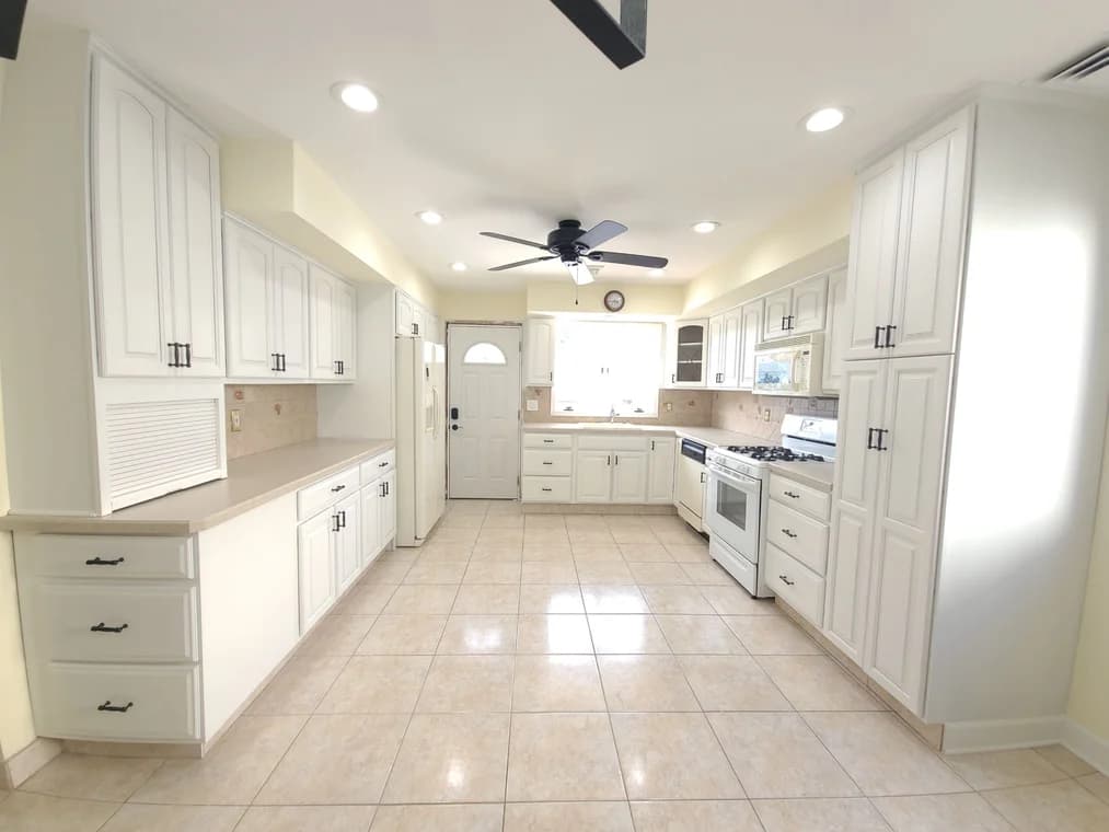 A bright, modernized kitchen with white cabinetry, tiled floor, and recessed lighting refinished by Hudson Paint Contracting.