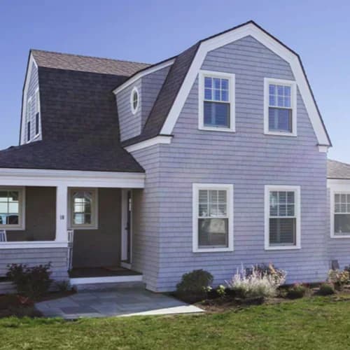This is an image from Promark Painting, located in Massachusetts. It shows a light gray shingle-style house with white trim and a dark roof, freshly painted to highlight its coastal architectural charm.
