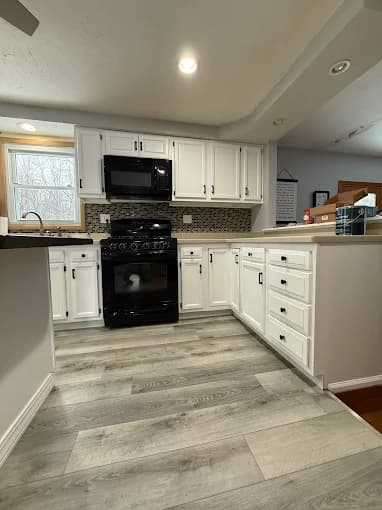 This is an image from Joseph Rivers Painting, located in Ohio. The photo shows a remodeled kitchen with white cabinets, light gray flooring, and a black stove and microwave.