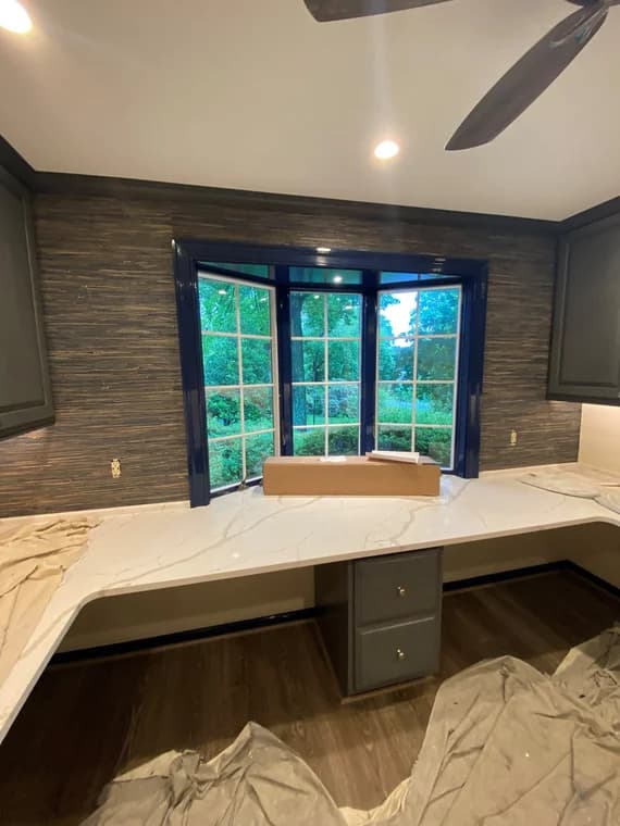 This is an image from Benner & Sons Inc company, located in Newtown Square, PA. The image is an interior home office under renovation with marble-look countertops, bay window, modern dark cabinetry, wood-look flooring, and fresh paint preparation.