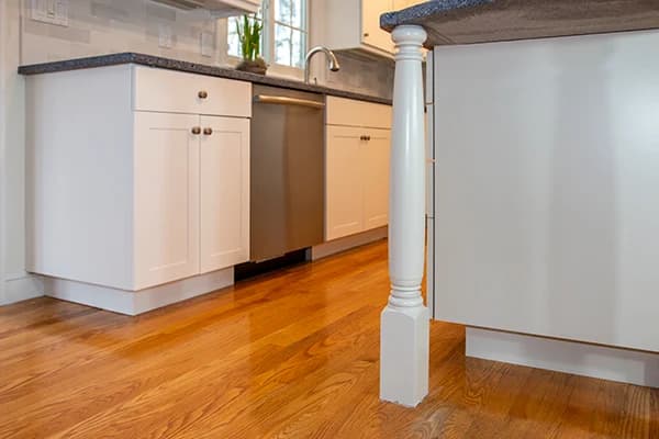 This is an image from Castle Complements Painting Co., located in Massachusetts. It highlights a modern kitchen with white cabinets, polished wooden floors, and stainless steel appliances.