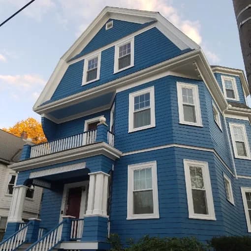 This is an image from CertaPro Painters of Boston. It shows a large three-story blue house with white trim and porch details, freshly painted for a bold look.