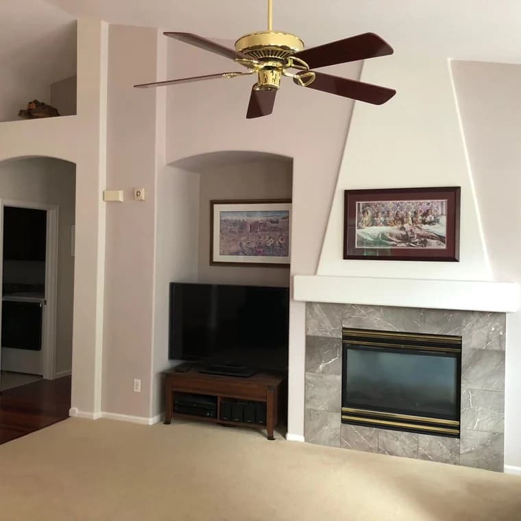 This is an image from Pro Classic Painting company, located in Aurora, CO The image is an interior living room with soft neutral wall paint, vaulted ceiling, gold ceiling fan, fireplace with stone surround, and decorative wall niches, painted by Pro Classic Painting
