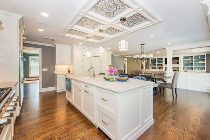 This is an image from Spectrum Painting, located in New Jersey. The photo shows a modern kitchen with white cabinetry, a large center island, detailed coffered ceiling, and warm hardwood flooring.
