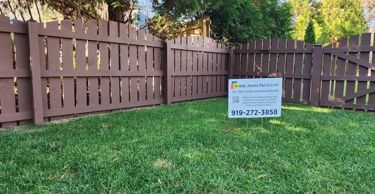 Exterior painting project by Grady Jones Paint in Garner, NC. The image shows a stained wood fence, green lawn, trees, and a company yard sign.