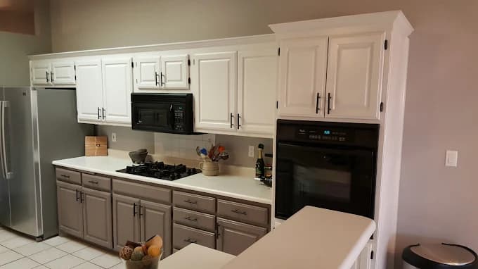 This is an image from Mike’s Pro Painting, LLC, located in New Mexico. The photo shows a modern kitchen with freshly painted two-tone cabinets—white uppers and gray lowers—complemented by stainless steel appliances and a clean, neutral wall color.