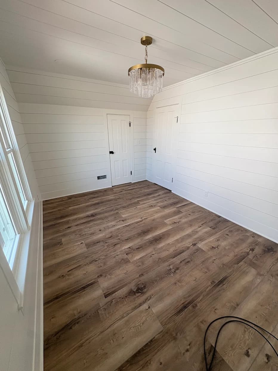 Interior painting project by Neff Paints in Warren, Illinois. The image shows an empty room with white walls, wood-look flooring, and a chandelier.