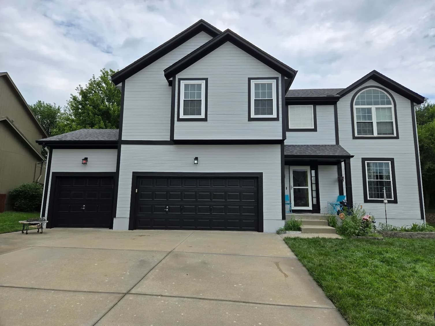 This is an image from PEMCO Painting Interior & Exterior Painter Overland Park. The image is an exterior home in Overland Park KS with newly painted light gray siding and bold black trim around windows, doors, and garage doors.