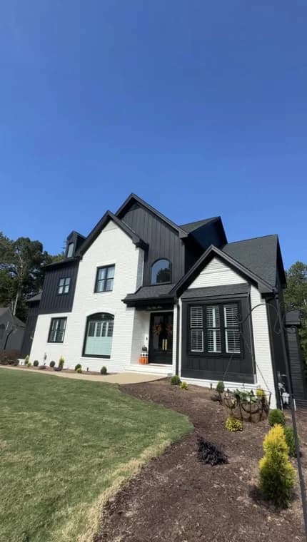 Exterior painting project by Mario's Painting NC in Clayton, NC. The image shows a white-and-black home with dark garage doors, green lawn, and planted beds.