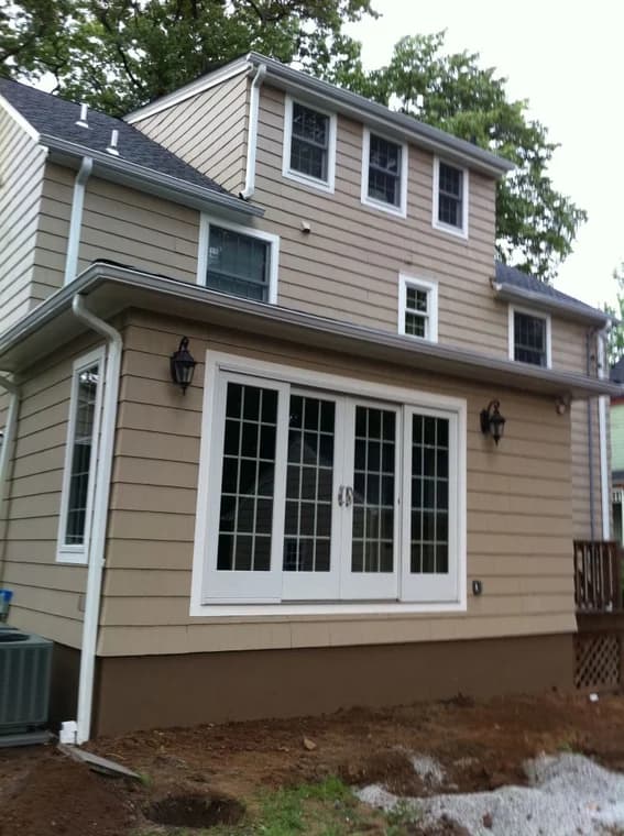 This is an image from JNG Painting LLC. It highlights the back of a tan-painted home with new siding and crisp white trim around windows and doors.
