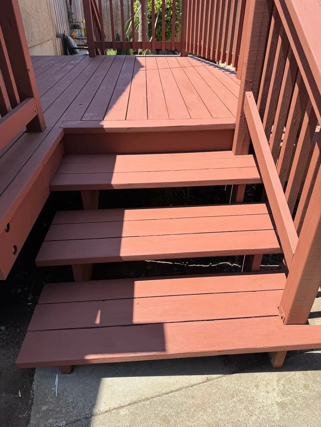 This is an image from Browder Painting Company, located in California. The image shows freshly painted exterior wooden deck stairs and railings with a smooth reddish-brown finish, clean edges, and evenly coated steps.