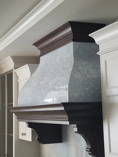 This is an image fromAncient Modern Finishes company, located in Bonita Springs, FL. The image is a custom kitchen range hood with polished decorative finish and dark wood trim by Ancient Modern Finishes