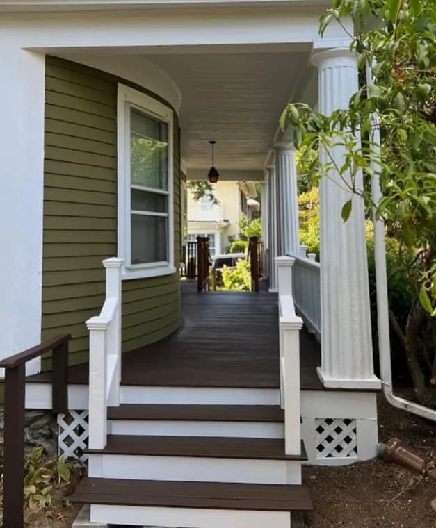 This is an image from Ulta Home, located in Massachusetts. It shows a freshly painted porch with white railings and columns, dark brown flooring, and a clean entryway, emphasizing attention to detail in finishing work.