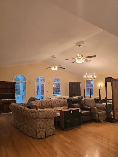 Interior painting project by Johnson Painting Co. & More in Kernersville, North Carolina. The image shows a living room with warm walls, hardwood floors, sofas, and ceiling fans.