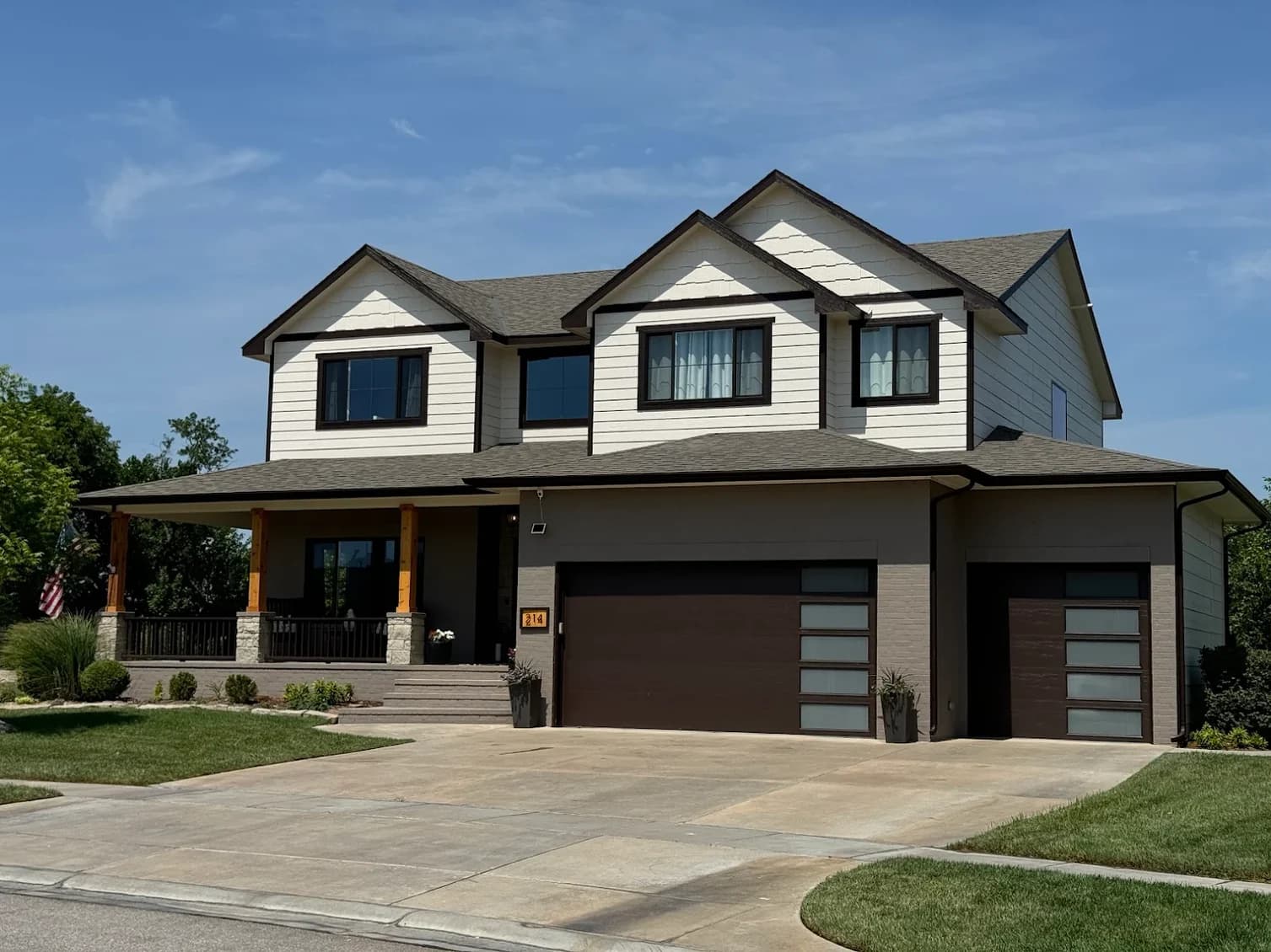 This is an image from Northwind Painting LLC. The image shows a two-story home with cream siding, dark brown trim, and freshly painted brown garage doors.