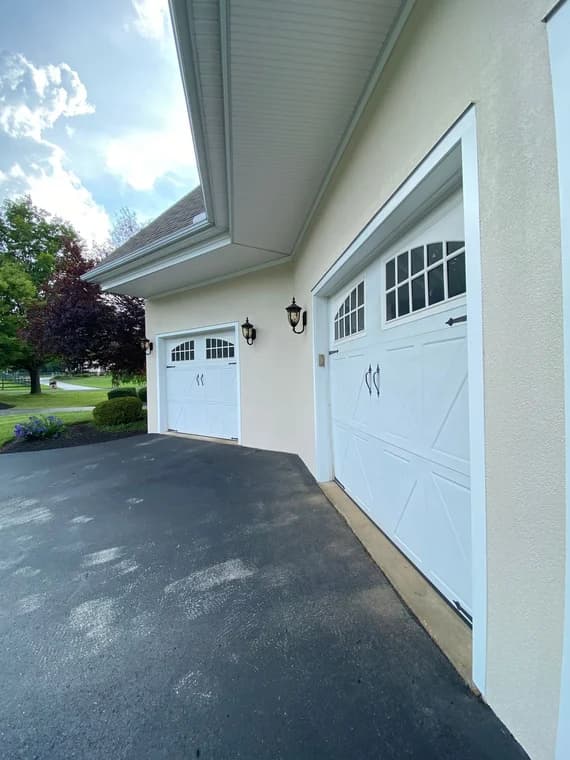 This is an image from MK Painting & Custom Finishes Co company, located in Schwenksville, PA. The image is a freshly painted stucco exterior with white trim and carriage-style garage doors featuring black accents