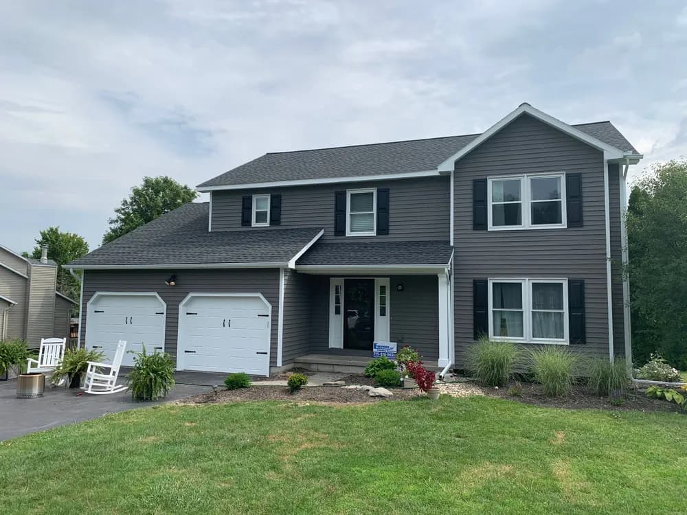 This is an image from Empire Painting Services LLC, located in New Jersey. The image shows a freshly painted two-story home exterior with gray siding, white trim, black shutters, and a clean, well-maintained front yard.