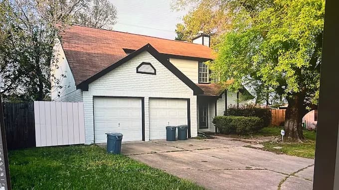 This is an image from Blue Painting, located in Texas. The image shows a two-story suburban home with a white painted exterior, contrasting black trim, a brown shingle roof, and a concrete driveway extending to a double garage.