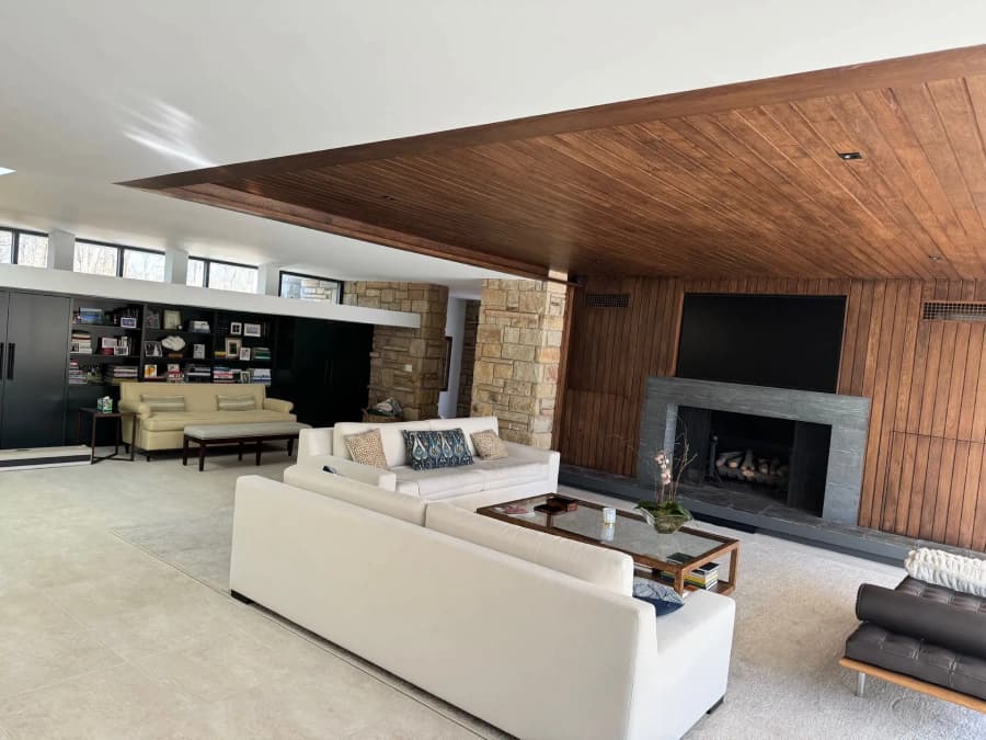 This is an image from Azul Painting Corp, located in New Jersey. The image shows a contemporary living room with painted walls, a wood-paneled ceiling, a fireplace, and custom built-in shelving.