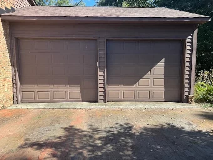 Exterior painting project by Richard's Painting of Concord in Concord, North Carolina. The image shows brown garage doors and matching trim on a brick garage.