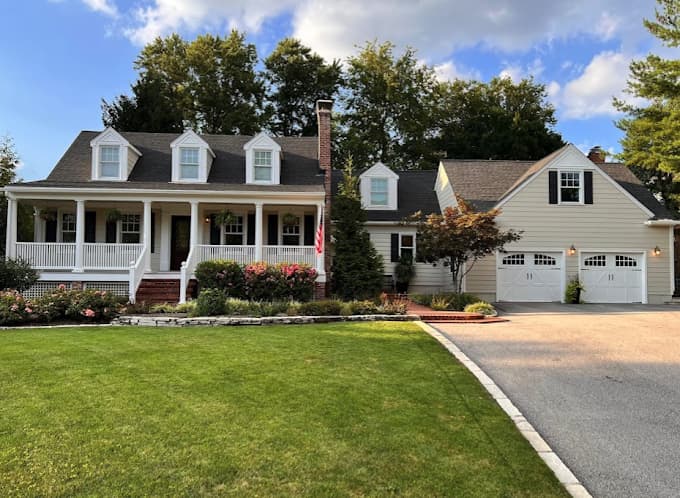 This is an image from SNL Painting Inc, located in Missouri. The image shows a freshly painted traditional two-story home exterior with light-colored siding, white trim, a covered front porch, and a detached garage, demonstrating professional exterior house painting services.